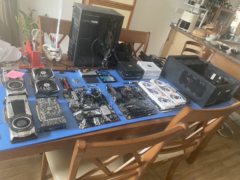 Real hardware workstation table with NVIDIA GPUs, motherboards, RAM, power supplies, and tools